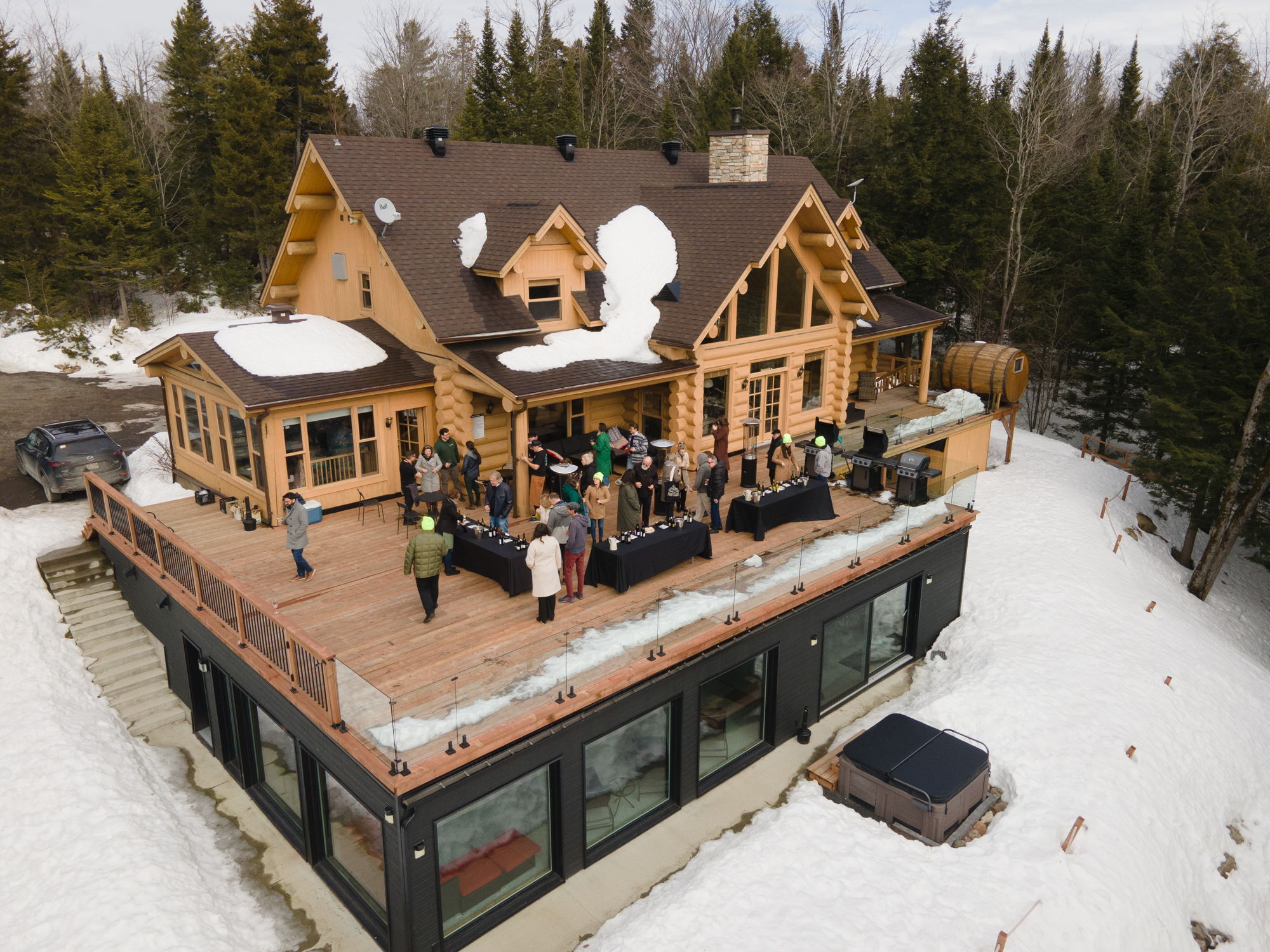 View of a luxury chalet covered in snow, surrounded by the forest, with people enjoying a wine tasting