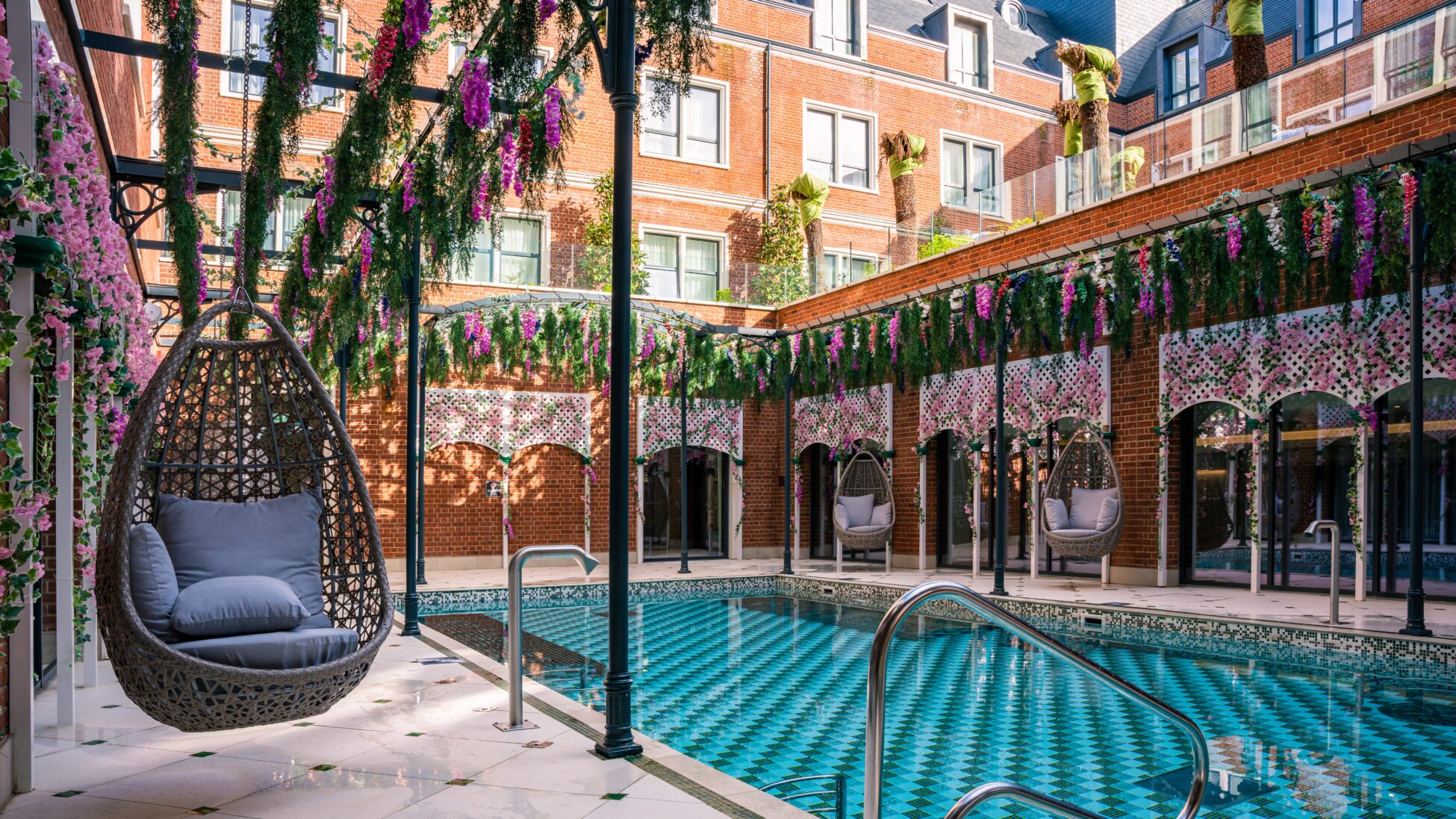 Luxurious outdoor pool area with hanging wicker chairs, floral decorations, and brick building backdrop