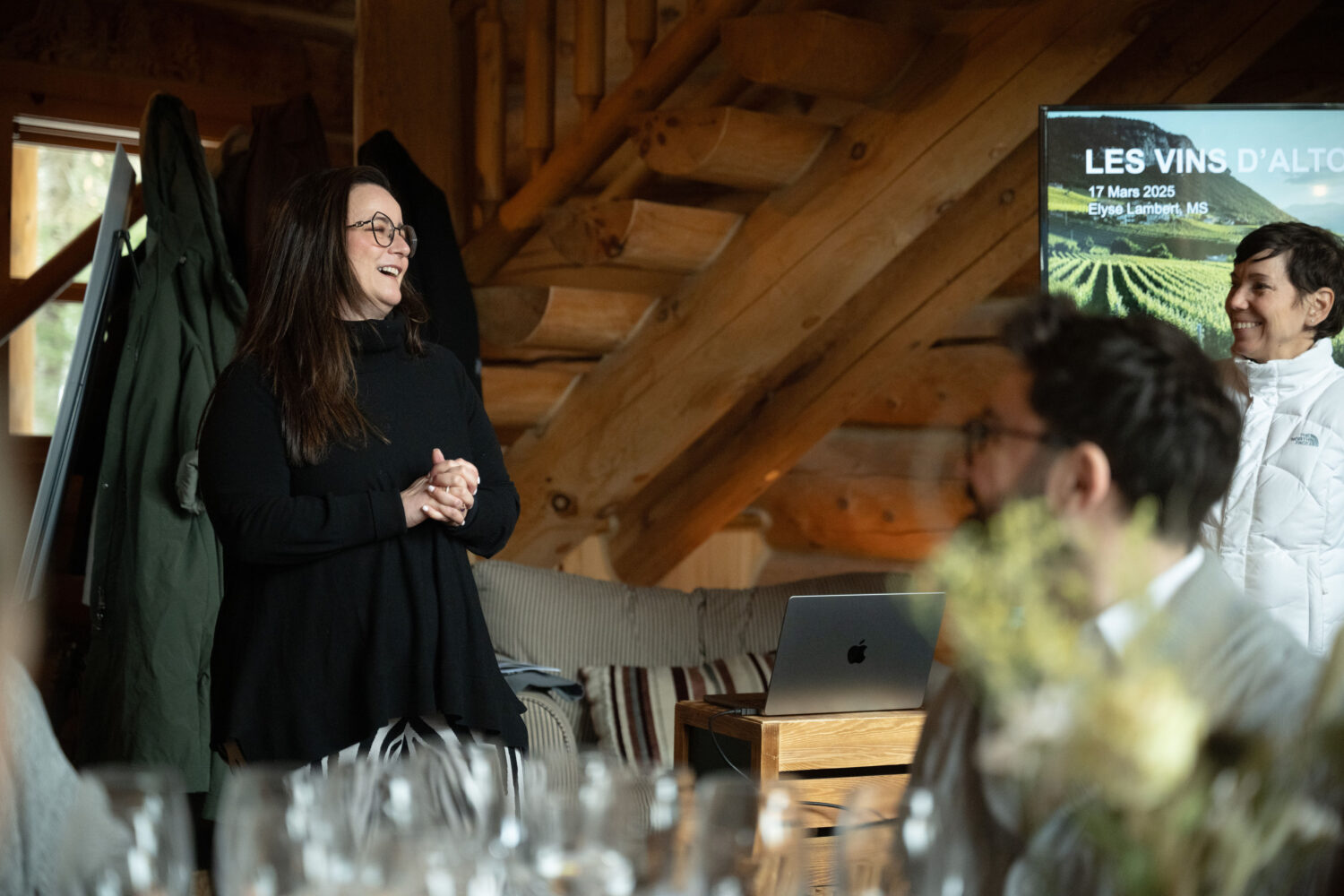 Woman smiling in front of small crowd and wine glasses