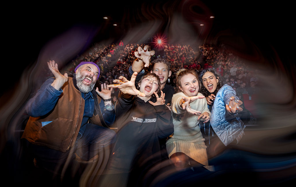 Group of excited people making playful, spooky faces and gestures in front of a packed theater audience
