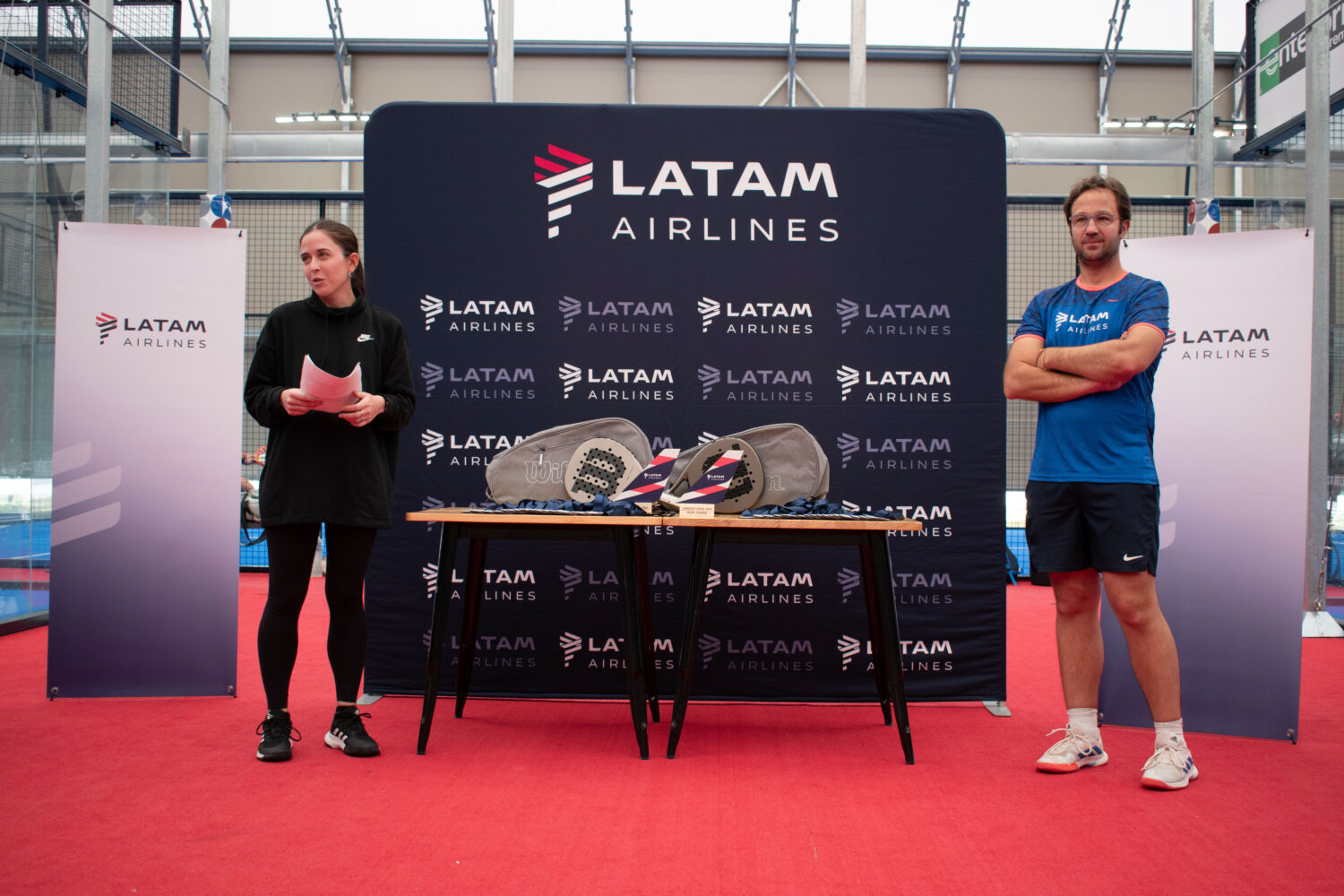 Two people standing next to board about Latam Airlines with padel equipment