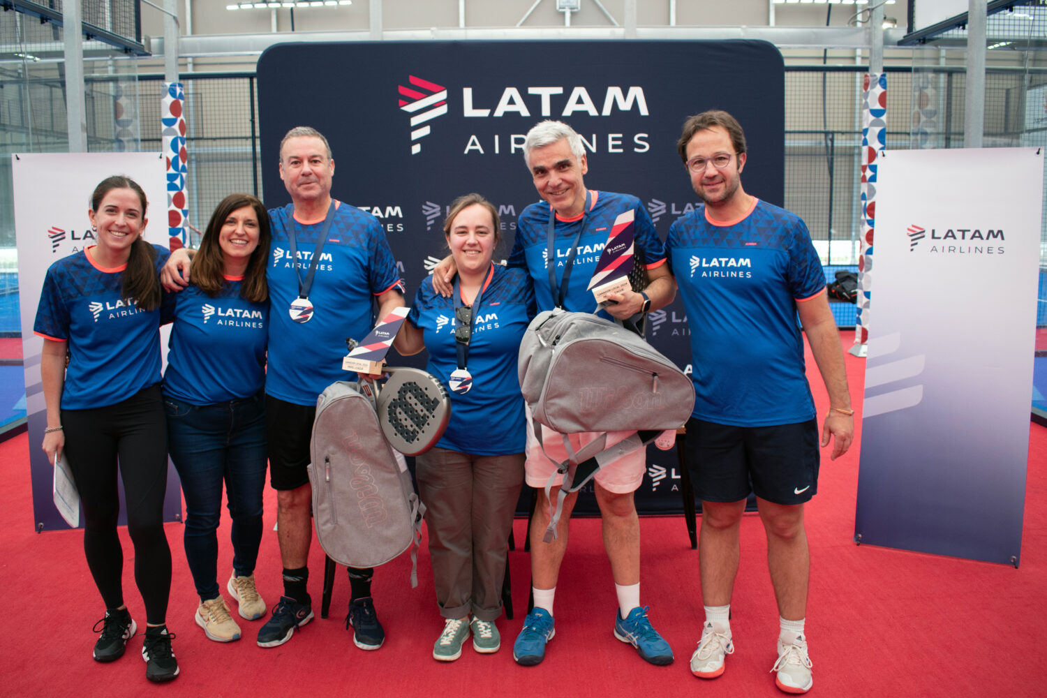 Four people standing next to board about Latam Airlines with padel equipment