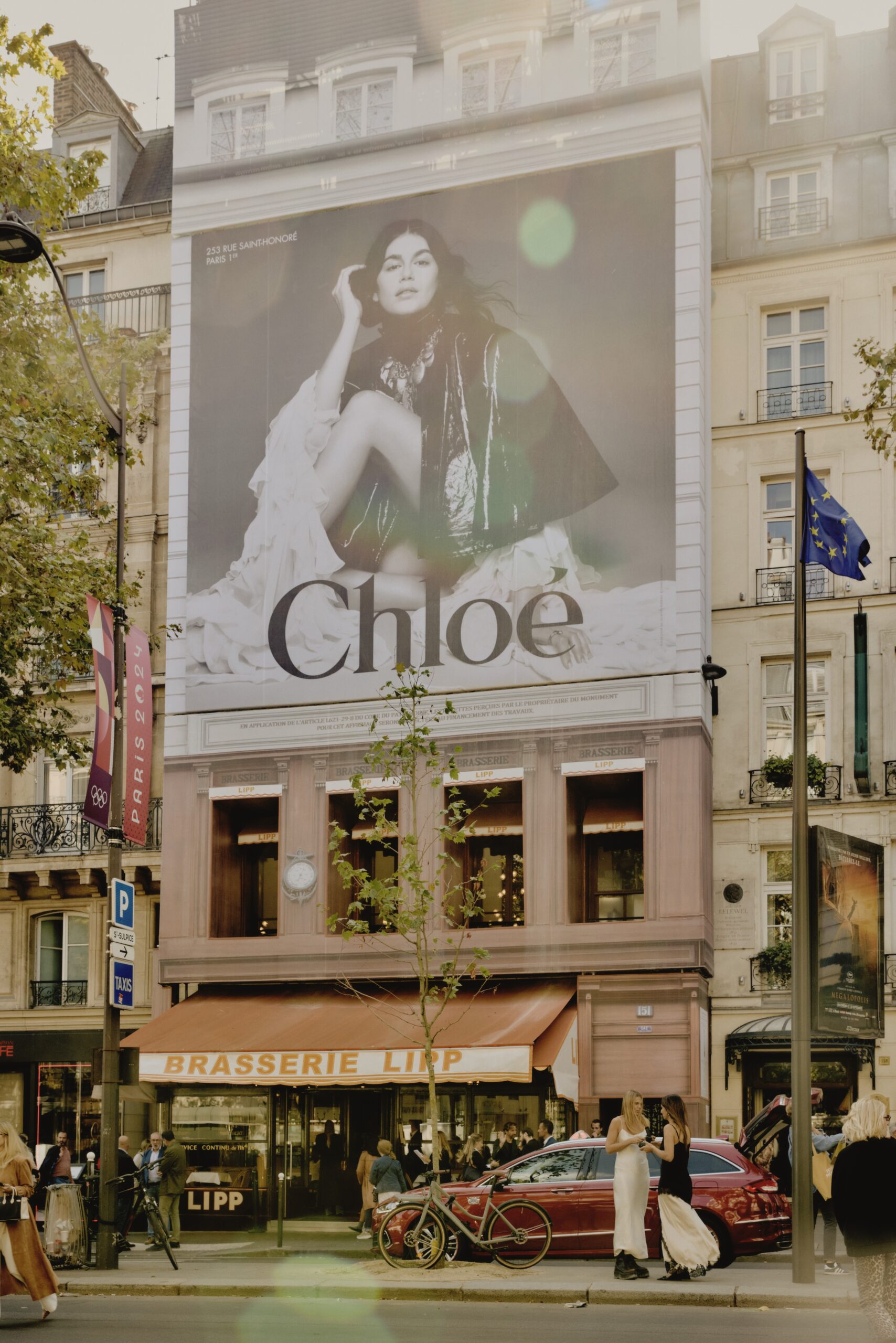 Large Chloé fashion billboard on building facade above Brasserie Lipp in Paris street scene