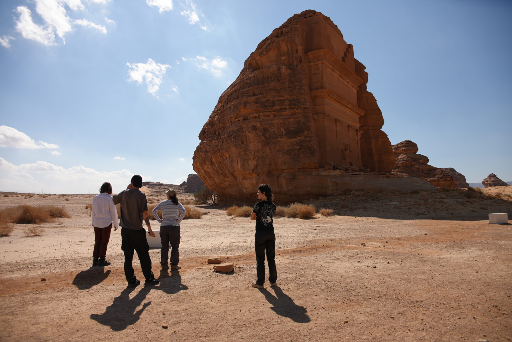 Four people standing next to cultural landmark in Saudi Arabia, bulding build into a mountain in the desert
