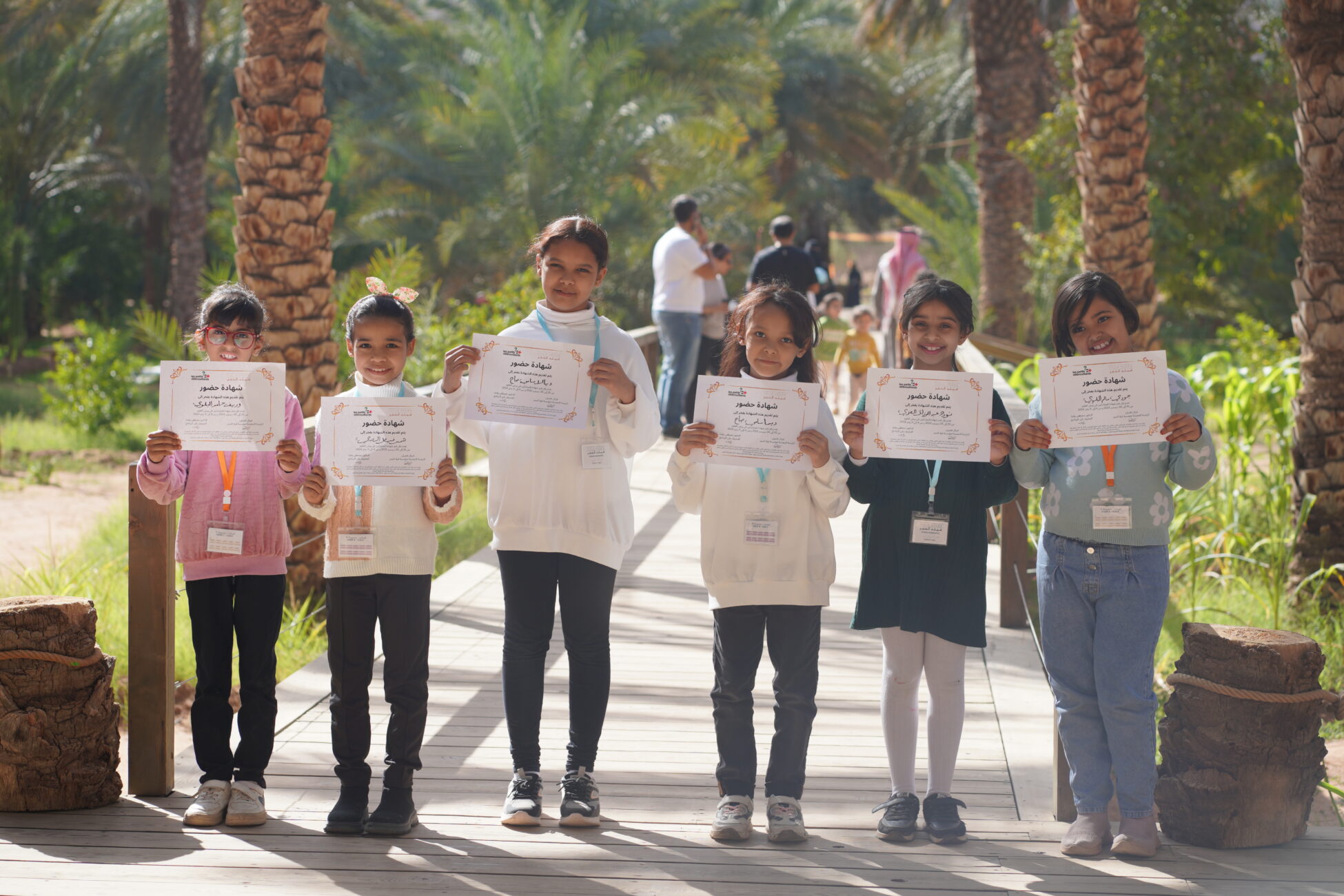 Six children holding certificates in green alley